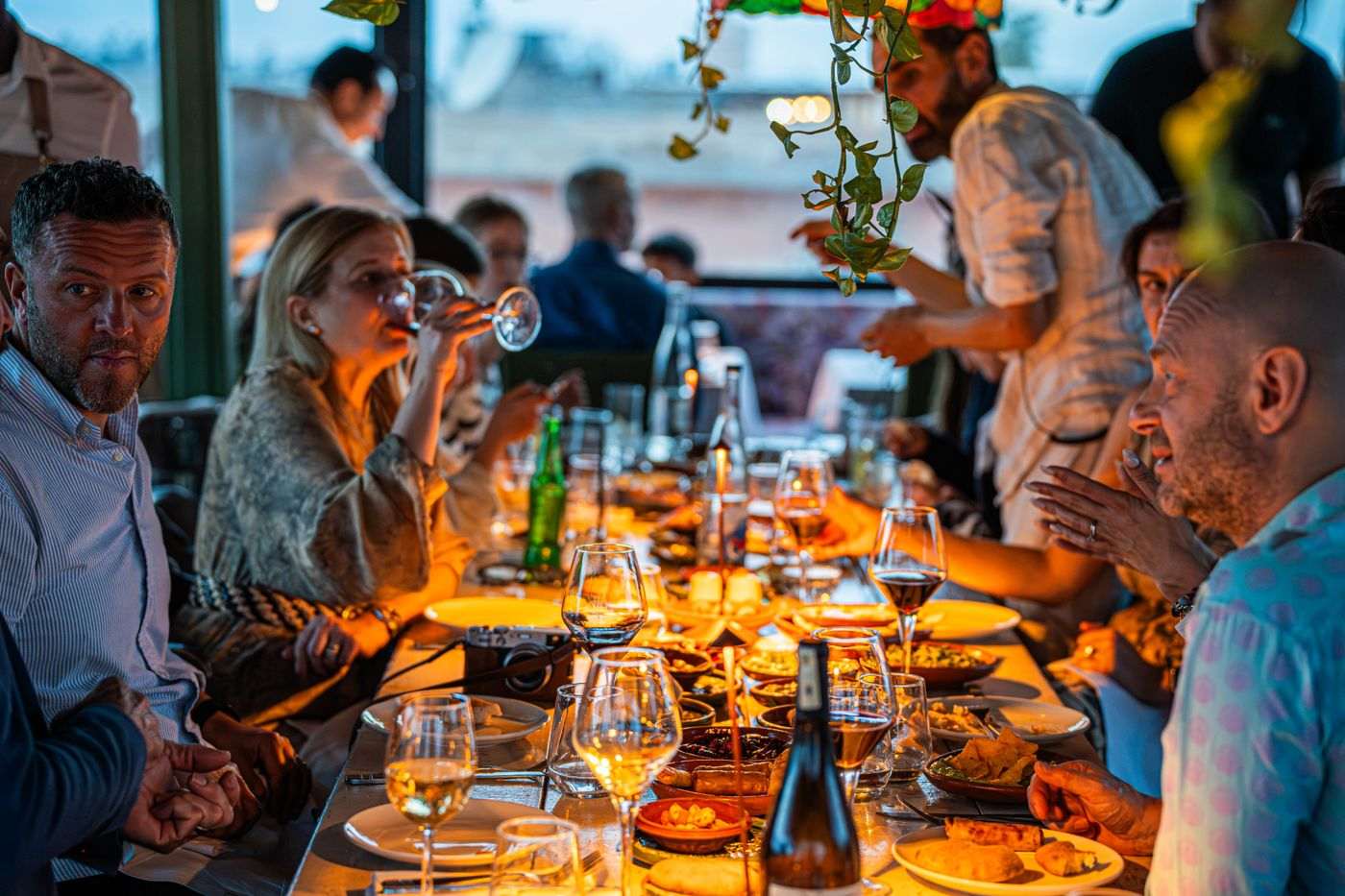 Friends around a long candlelit restaurant table with wine and small plates